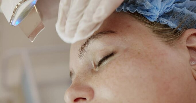 Woman receiving ultrasound facial peeling at beauty salon, closeup. Facial cleansing with ultrasonic scrubber. Cosmetology and face skin care. Facial treatment