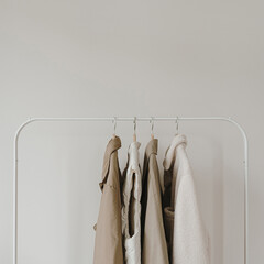 Warm autumn seasonal women's clothes on hanger over white wall. Neutral beige jackets and coat....