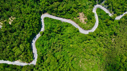 View from above on a winding road passing through the mountain slopes through a dense tropical forest. Road through the jungle. Aerial view of the road through the forest.