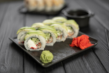 Uramaki sushi roll with smoked eel covered by avocado and sesame seeds served on black slate board