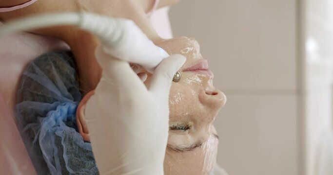 Closeup of beautician hands doing facial microcurrent treatment with apparatus on beautiful female face in beauty wellness salon. Using electrical impulses in cosmetology. Vertical video.