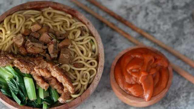 Indonesian chicken noodles called mie ayam topped with chicken meat and green mustard served in a bowl with red spicy sauce