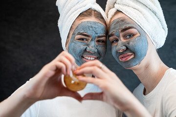 Two happy women sister wear white bath towel apply  beauty facial mask and hold pieces of orange
