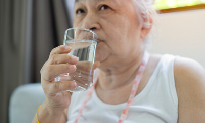 Active senior woman drinking fresh water from glass after domestic sports workout