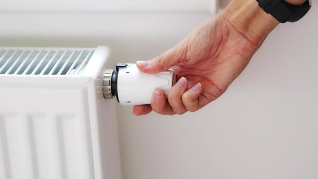 A woman's hand turns the battery heating knob. Heating in an apartment, at home. Heating prices.