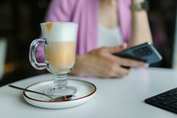 Business woman sitting in cafe with a laptop and smartphone, In the foreground, a tall glass with latte coffee close-up.