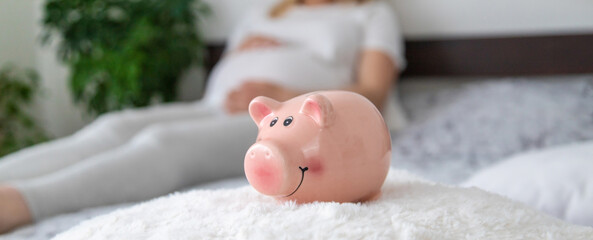 A pregnant woman holds a pig bank in her hands. Selective focus.