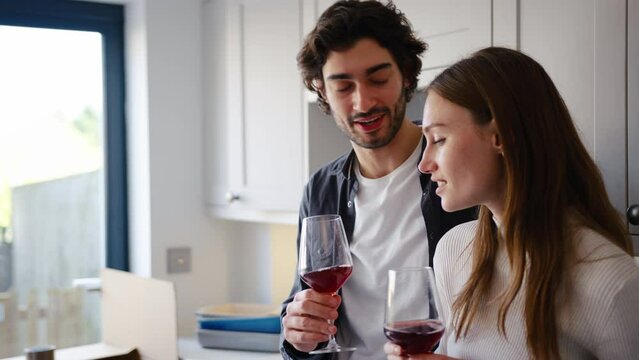 Excited couple celebrating with glass of red wine in kitchen of new home as they unpack boxes on moving in day together - shot in slow motion