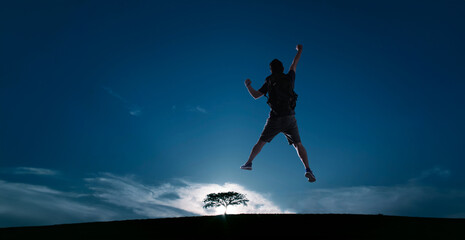 Silhouette image of young guy cheer and jump up with cold tone sunset landscape . success, leadership and achievement concept .