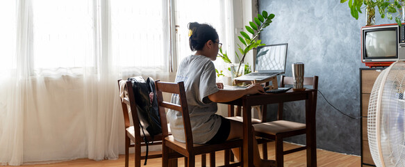 Professional businesswoman working at her home on laptop, young female manager using mobile computer device while sitting at dining table.
