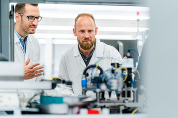Colleagues in electronics factory watching machine work