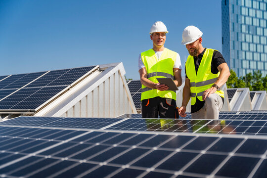 Two technicians using tablet PC on the roof of a company building with solar panels