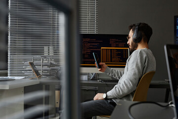 Computer programmer using smart phone at desk