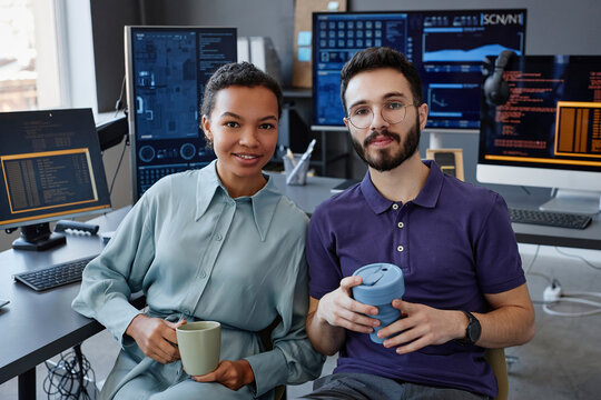 Smiling IT professionals sitting together with coffee cups in office