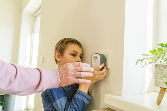 Grandfather assisting grandson to install timer in electrical outlet on wall