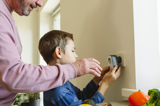 Grandfather and grandson installing timer in electrical outlet on wall