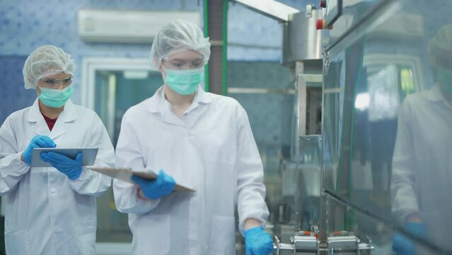 Female factory worker check machine systems at the industrial factory. Women working in clean rooms for beverage and food production. Female worker recording data at the control panel.