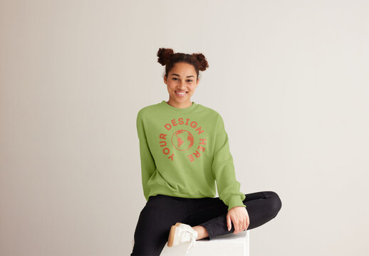Mockup of woman wearing customizable color sweatshirt sitting on plinth with leg bent