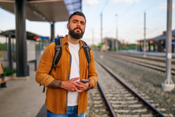 Adult man is standing at railway station and waiting for arrival of train.