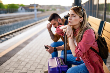 Anxious and tired couple sitting at railway station and waiting for arrival of their train.