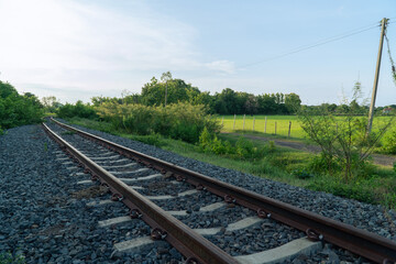 Obraz premium The railway through the lush green rice fields, amidst the sunshine, in the rural northeastern region of Thailand during the rainy season. 