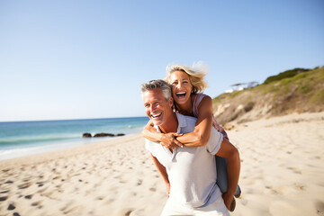 gorgeous mid age Couple enjoys a piggyback ride at the beach in summer