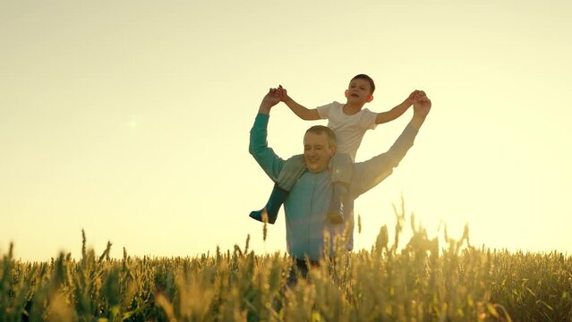 father carries child shoulders. happy father walking with little son wheat field. farmer shows his child fields wheat sunset field. summer harvest. Child dreams becoming airplane pilot. shoulder