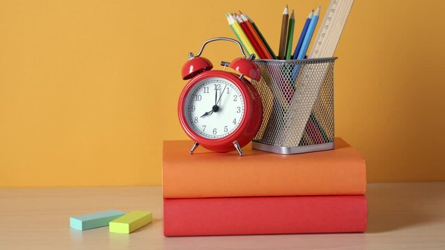 School background. School supplies, a book stack, and an alarm clock are on the desk.