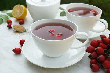 Fresh rose hip tea, lemon and berries on marble table. Vitamin C drink on white background. Anti-cold tea is an antioxidant for health in the flu season of colds. Side view.