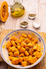 Diced pumpkin pieces in a bowl, with spices and olive oil