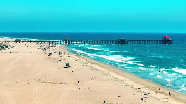 Drone flying over Huntington Beach looking at the Pier and some large waves breaking on the shore.