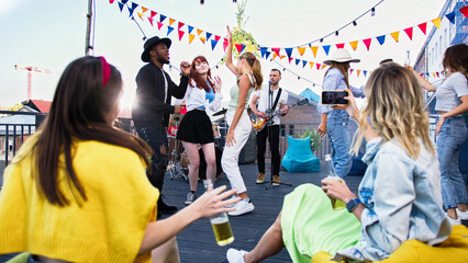 Attractive smiling young carefree women drinking beer and making selfie during summer party on terrace. Friends having fun and dancing on a rooftop party.