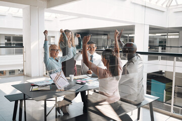 Excited group of businesspeople cheering around an office table