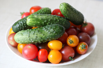 Fresh red, pink and yellow tomatoes and green cucumbers on the white plate