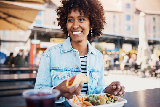 Young woman smiling and eating tacos on the patio of a restaurant