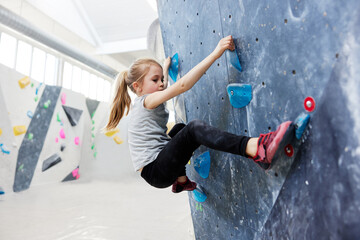 Girl climbing on a wall in bouldering gym