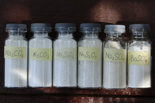 White inorganic reagents in glass tubes: sodium and potassium carbonates, sodium silicate, sodium thiosulfate, sodium and barium sulfates are in a wooden table. 