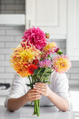 A woman holding a bouquet of bouquet of dahlia flowers a light background.