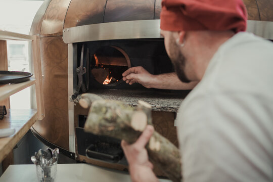 Cook putting wood in the oven of a pizzeria kitchen