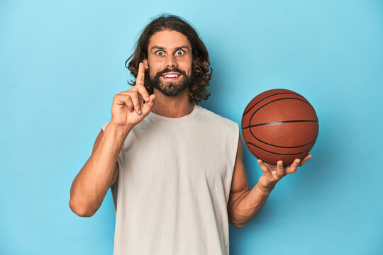 Bearded man with basketball in blue studio having an idea, inspiration concept.