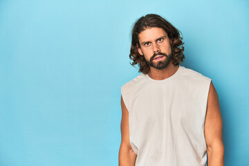 Bearded man in a tank top, blue backdrop shouting very angry, rage concept, frustrated.