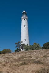 Fototapeta na wymiar Big white lighthouse on Rottnest Island. Wadjemup Lighthouse at Rottnest Island, Western Australia. Tall white historic lighthouse in front of a perfect blue sky. Western Australia tourist destination