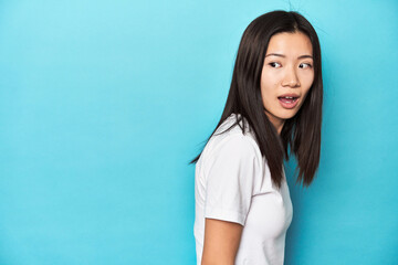 Young Asian woman in white t-shirt, studio shot, looks aside smiling, cheerful and pleasant.