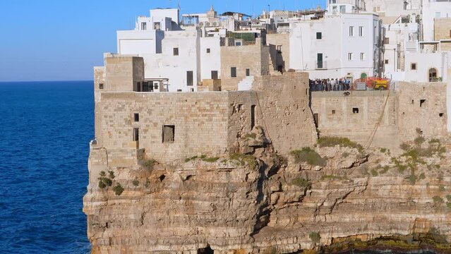 Video sunset in shot at golden hour in Polignano a Mare showing the city on the cliffs with the sea and blue sky.