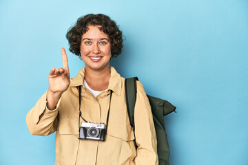 Young traveler woman with vintage camera showing number one with finger.