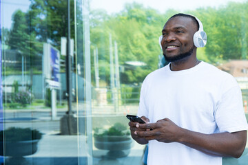 Stylish young African-American man listening to music in headphones with a smartphone in his hands