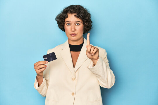 Young woman with credit card, elegant white blazer showing number one with finger.