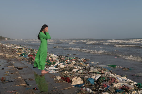 woman in green dress standing in plastic waste washed upon shore near ocean in Vietnam