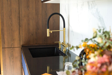 Stylish flexible mixer in gold color in the kitchen. Black tabletop