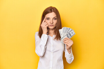 Redhead with dollar bills, cash in hand showing a disappointment gesture with forefinger.